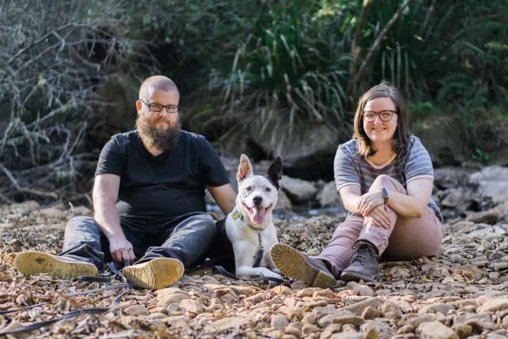 Robey, Mel and Oakey the dog sitting on a rocky creek bed in the bush